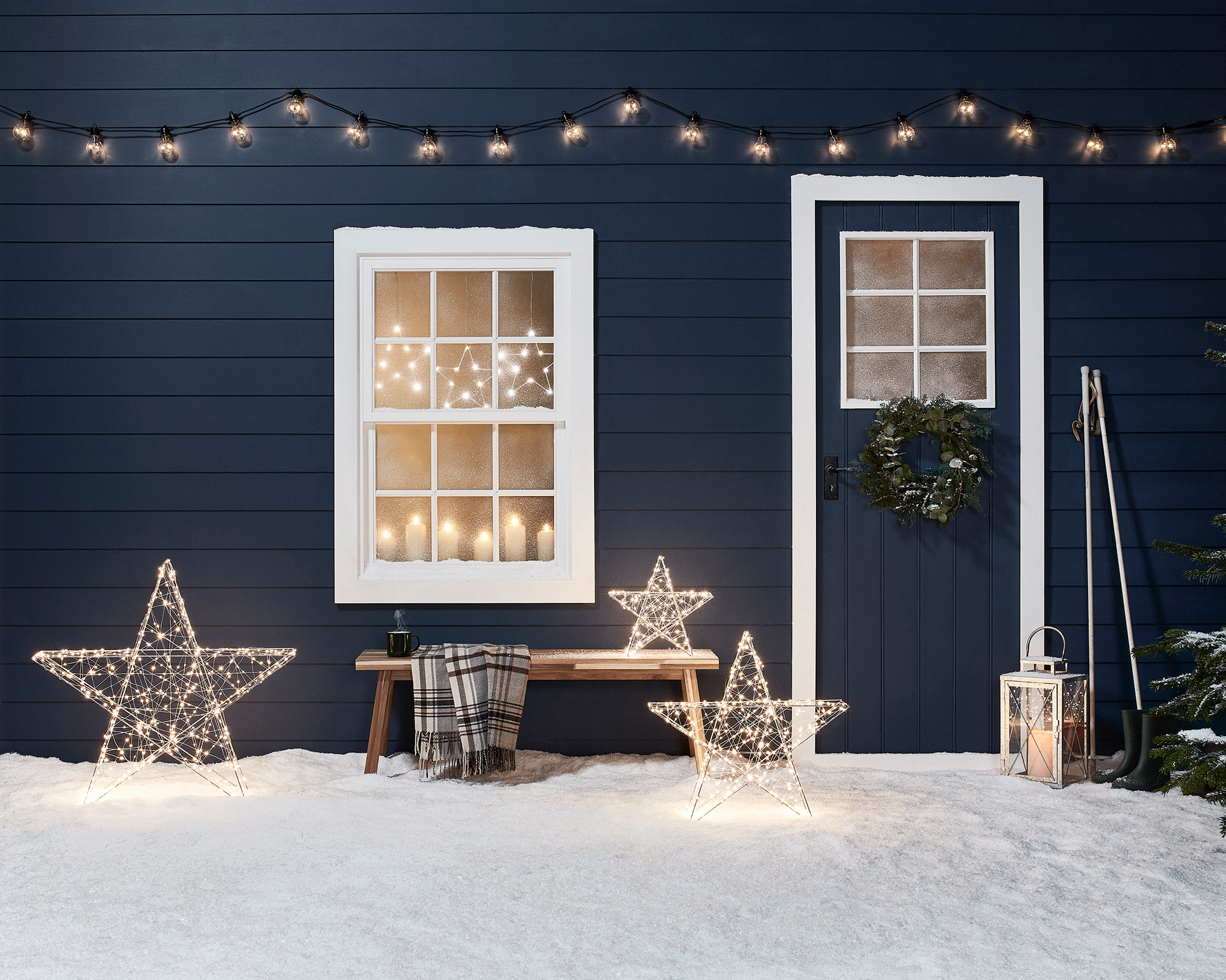 Outdoor Christmas decor at a cabin with three light up stars and fairy lights