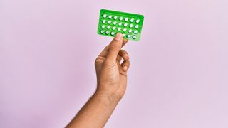 Young hispanic hand holding birth control pills over isolated pink background.