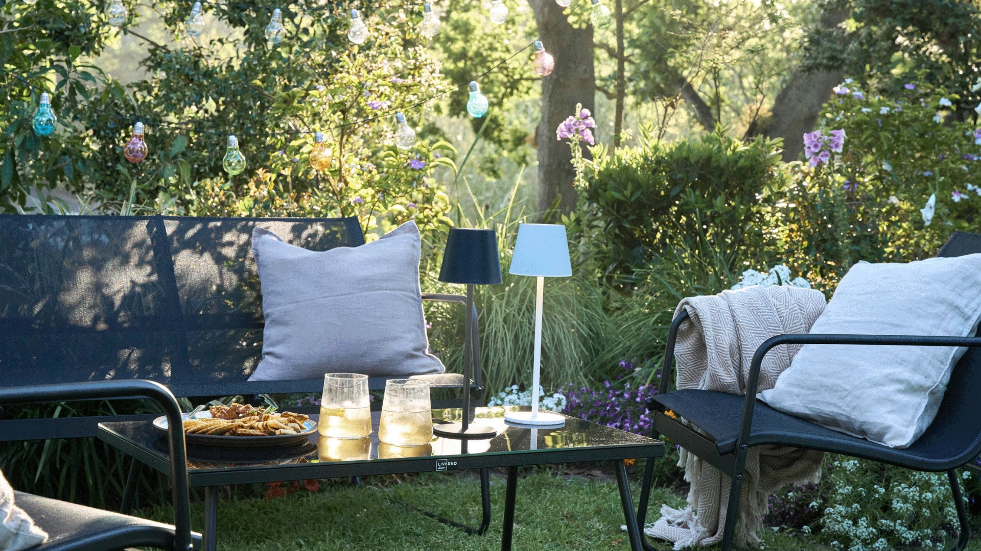 Lidl garden furniture sofa set with cream pillows, blankets and a black and a white rechargable light.