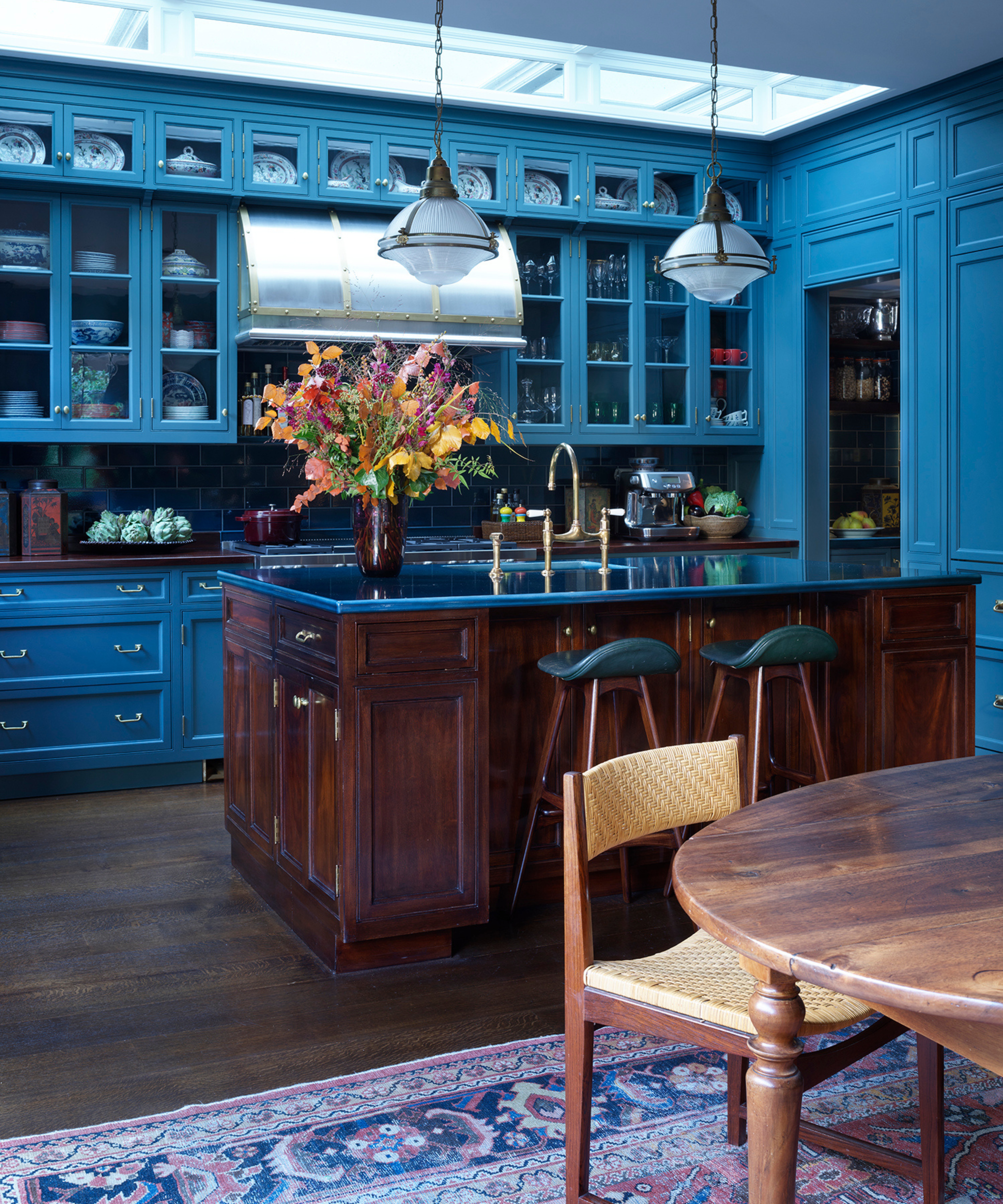 Vibrant blue kitchen with glass-fronted cabinets, a dark wood center island, dark countertops, and a large colorful floral arrangement
