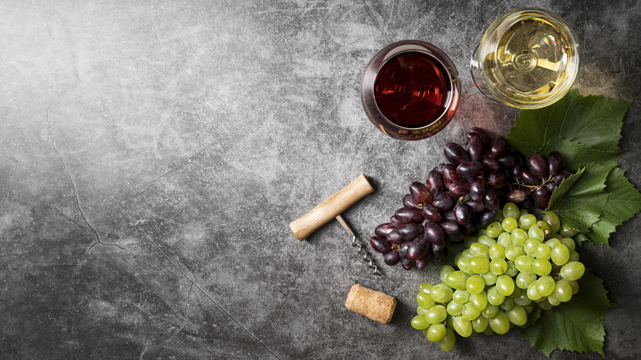 Red and white grapes, a glass of wine and a corkscrew on a marble slab