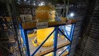 A big orange fuel tank stands vertical surrounded by scaffolding 