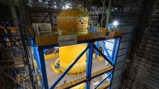 A big orange fuel tank stands vertical surrounded by scaffolding 