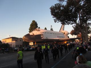 The rising sun bathes space shuttle Endeavour in a golden glow as it rolls down Martin Luther King Jr. Boulevard on Oct. 14, 2012.