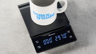 the KitchenTour black coffee scale with a digital LED screen and 0.1g weight accuracy is photographed against a blue background