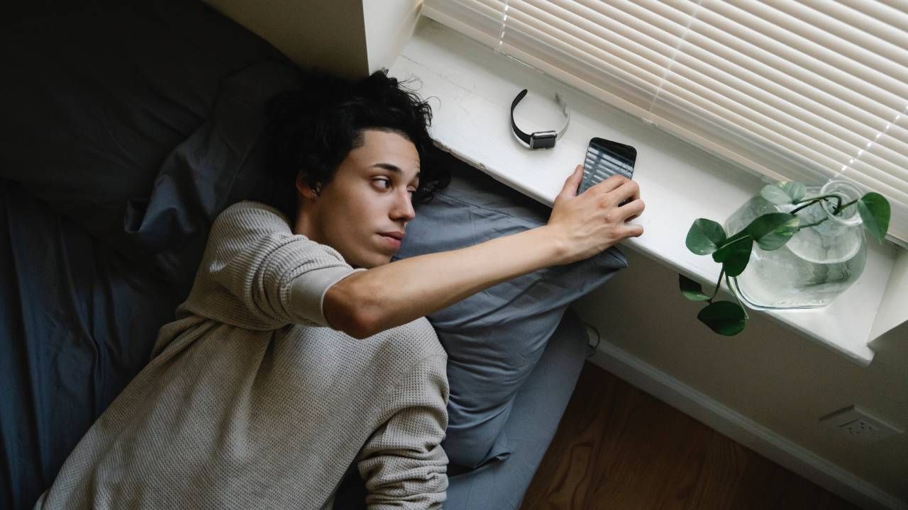 A man in bed reaching for his phone