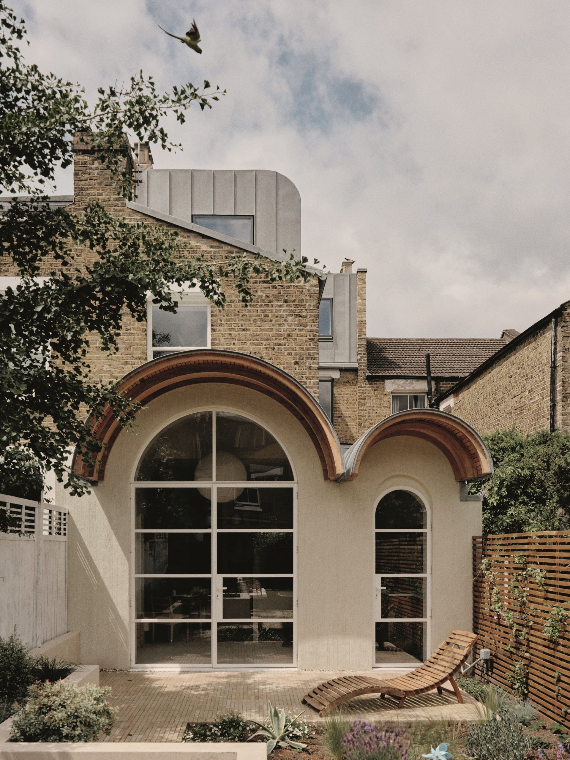 arched extension on London terrace with steel-frame doors, a sun lounger, and brick garden floor