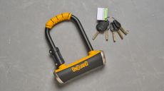 Onguard Pitbull mini lay on a grey concrete floor, alongside it keys. 