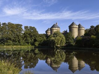 View of Château des Lassay in Mayenne, France, standing on a rock, above a pool.