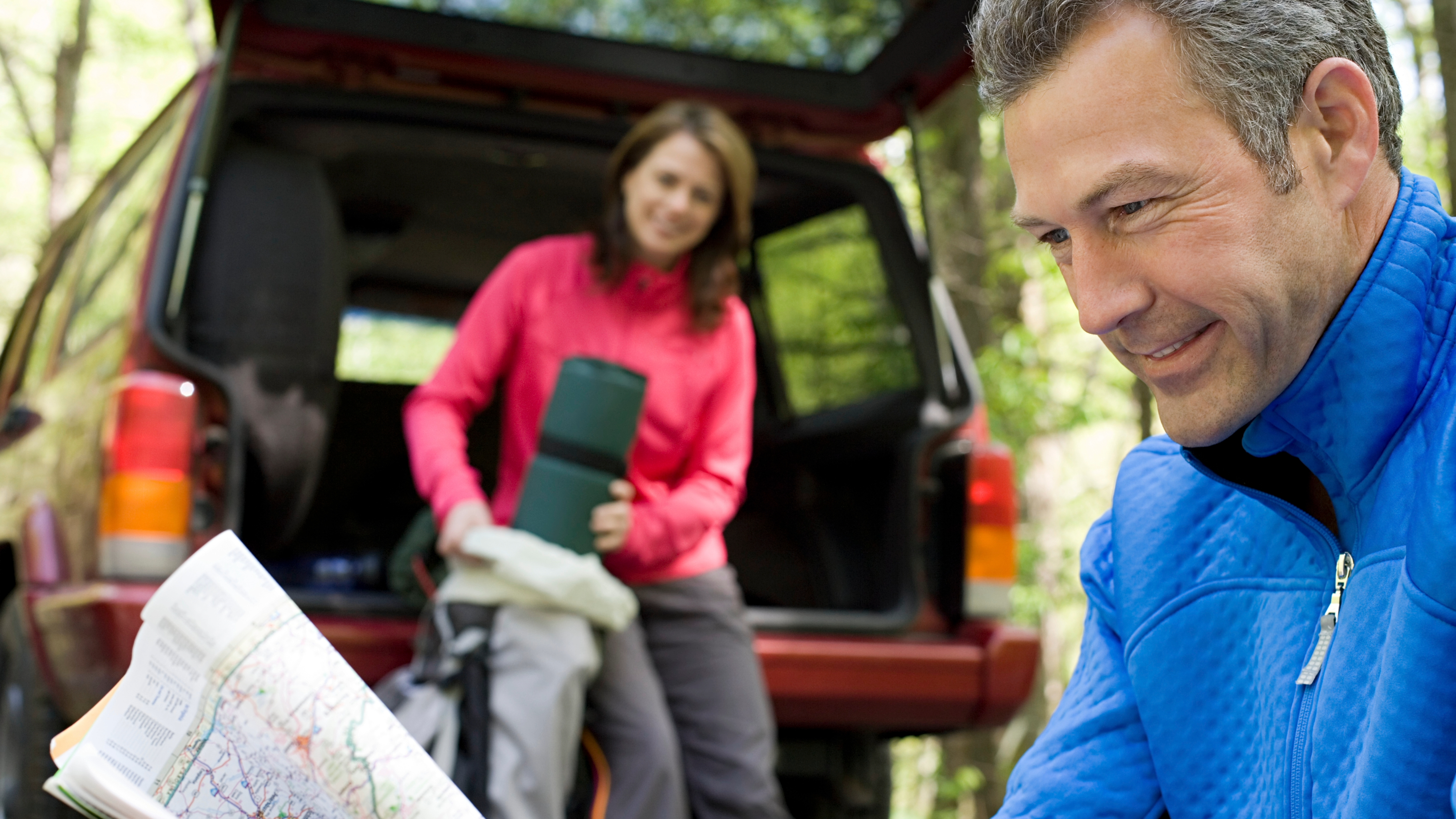 Man looking at a map while his wife is sitting in the truck of their SUV