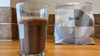 Glass of protein shake made with chocolate Bulk Pure Whey Protein next to packet