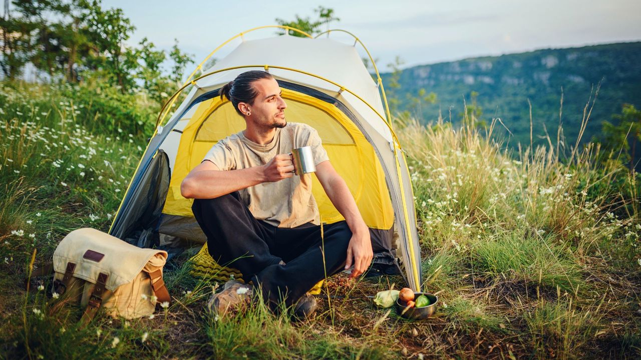 Man sitting on the grass outside his tent having a hot drink