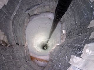 An IceCube sensor, attached to a "string," descends into a bore hole in the Antarctic ice.