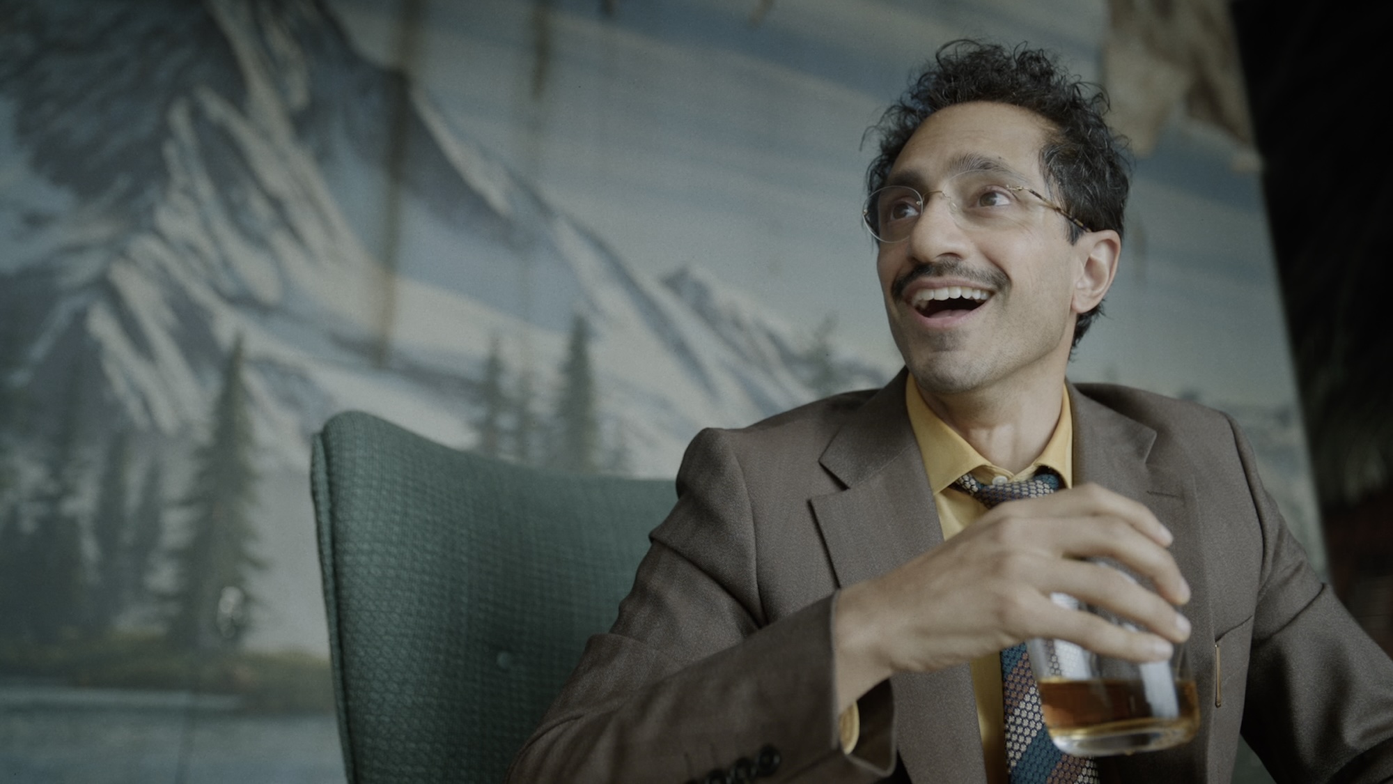 Riz Ahmed smiling with a drink in Digger