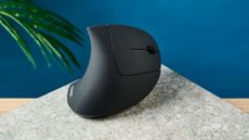 The Anker 2.4G Wireless Vertical Ergonomic Mouse on a stone surface with a blue wall in the background
