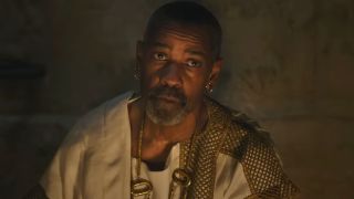 Denzel Washington sits stoically in the firelight in Gladiator II.