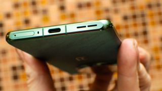 OnePlus 12 hålls upp av en hand för att visa undersidan och mobilens laddningsport.