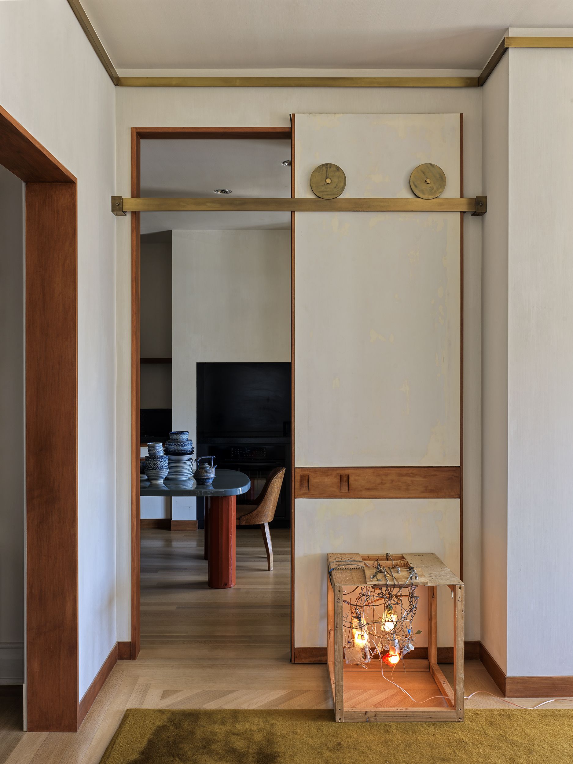 A white sliding door next to a piece of bulb art is open to reveal a kitchen with a blue and red kitchen table or island