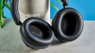 the soundcore space one pro headphones; a closeup photograph of a pair of black over-ear headphones with cushioned cups and a soft headband, photographed in front of a blue background