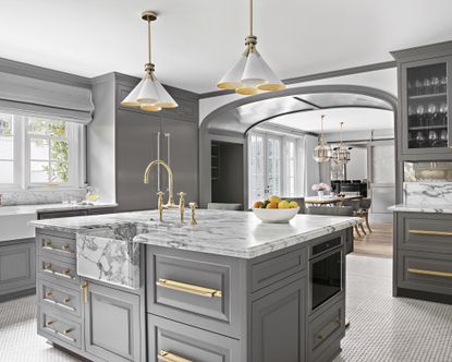 A kitchen with coned chandelier fitting over grey island with marble counter