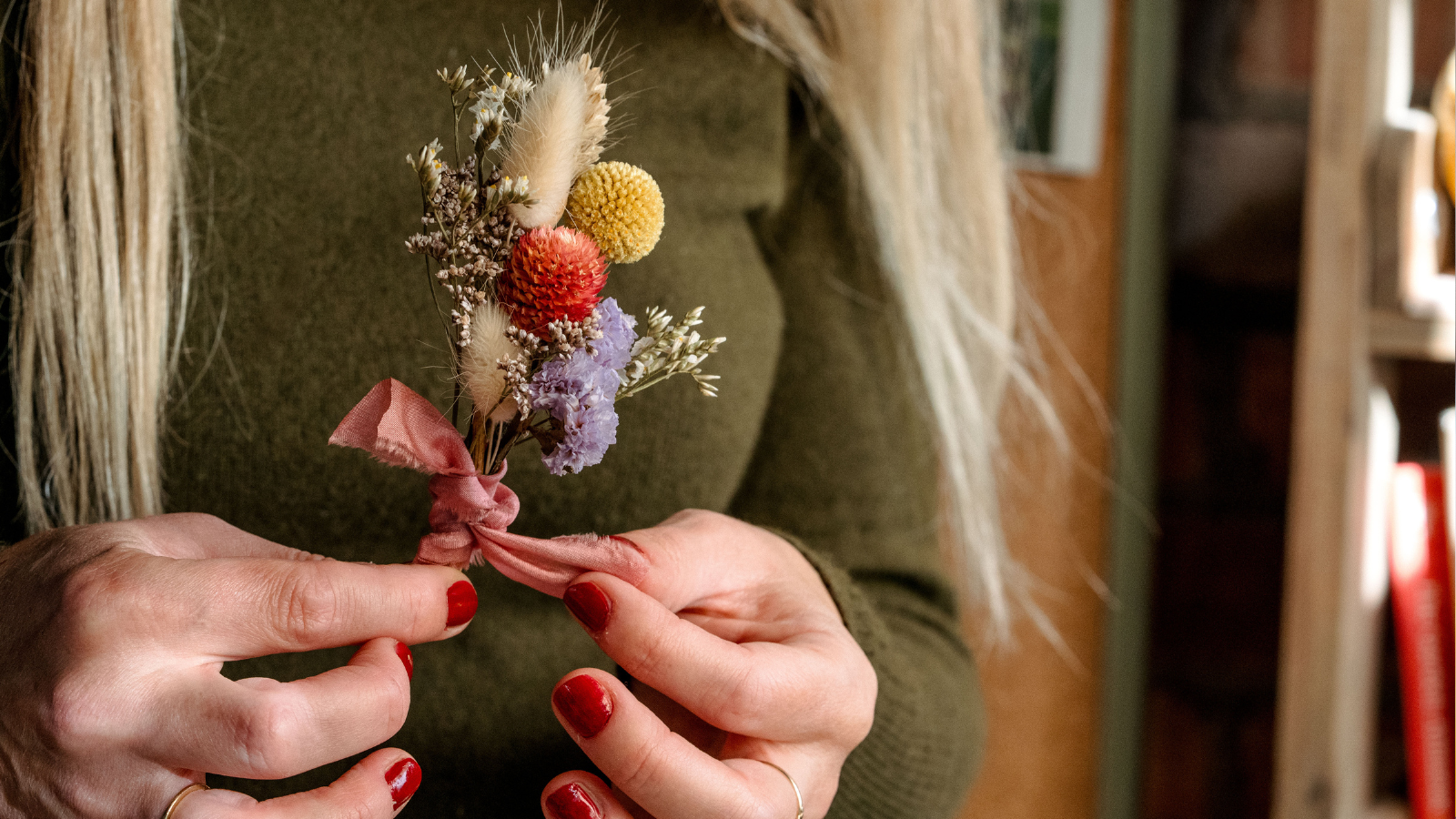 Hands holding a dried flower corsage with a pink silm ribbon