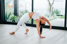 A woman in white activewear doing yoga next to a window.