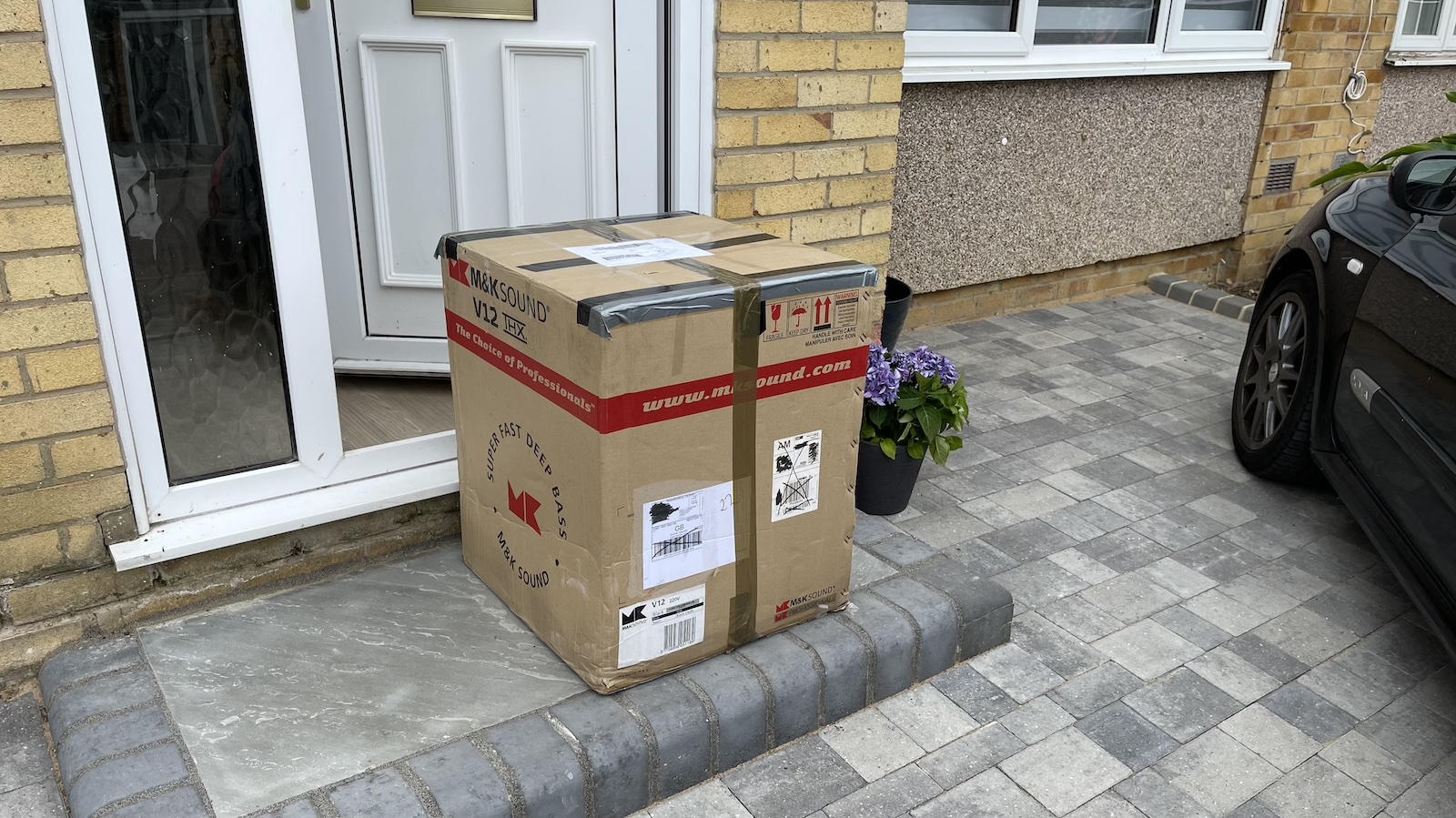 A photo of a large, boxed subwoofer on the doorstep of someone's house