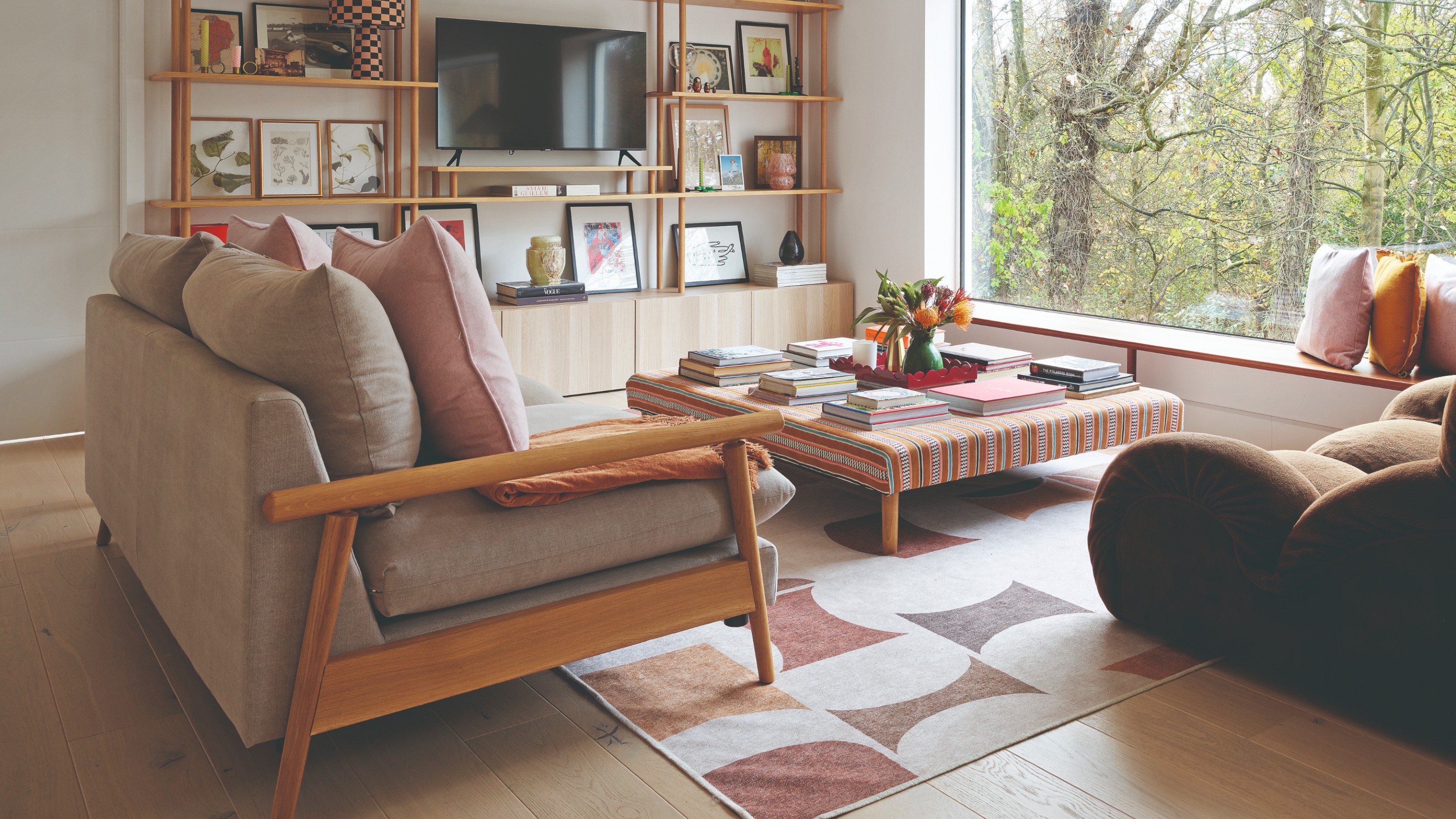 A living room with a midcentury-style sofa with exposed wood armrests and feet and a patterned ottoman used as a coffe table