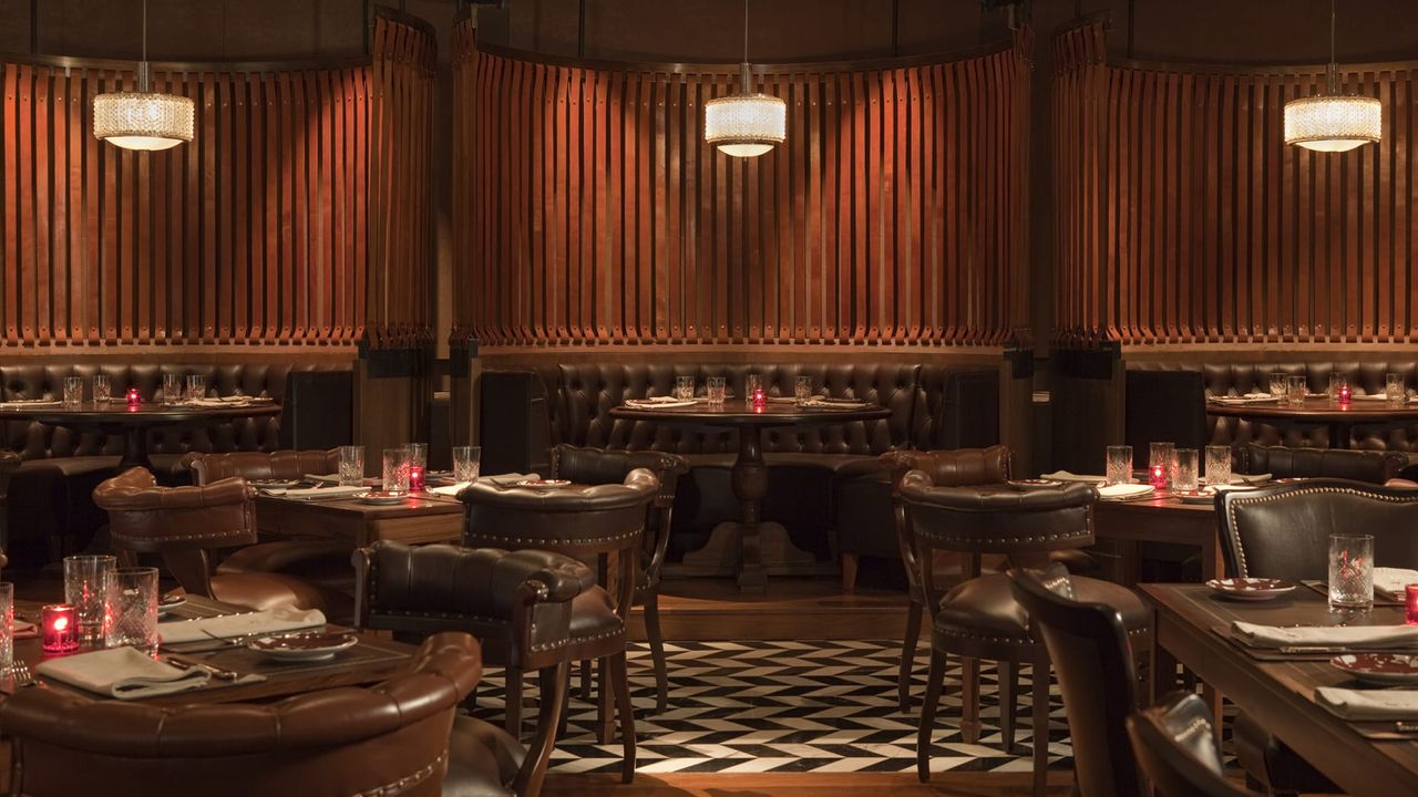 Image of a formal dining room at Four Seasons Buenos Aires. The walls are textured red wood with dark green leather seating