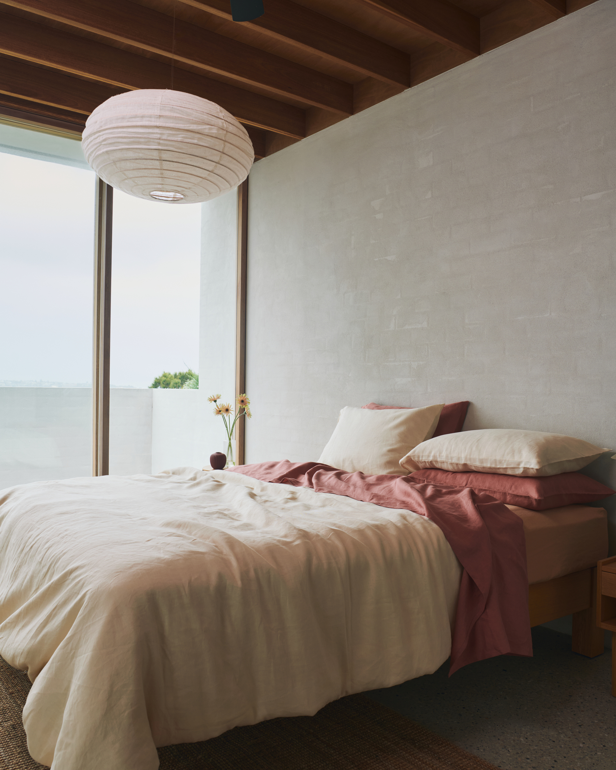 Image of a minimalist bedroom with bedding that is a faded butter yellow and terracotta red.