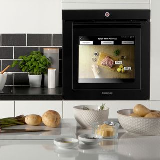 Black tiles in black and white kitchen with built-in Hoover oven behind granite top with food items on it