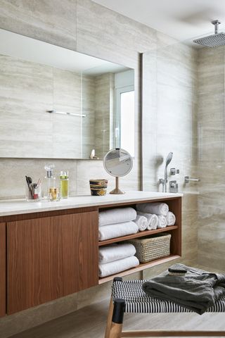 make up vanity in bathroom with drawers underneath, walk in shower with glass door, mirrors, stone floor and wall tiles