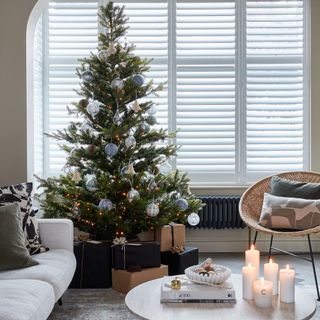 A modern, minimalist living room with a decorated lit Christmas tree and lit candles on a marble coffee table