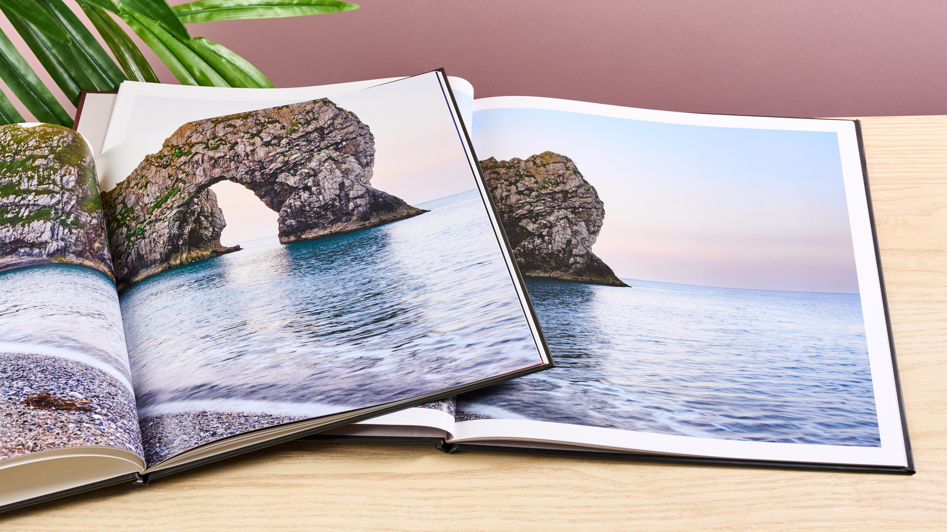 The Once Upon photo book sits on top of the Blurb photo book. Both pages show a two-page spread of the same image of a pebble beach and cliffs.