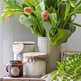 Candles and jars on a wooden shelf beside a vase of tulips