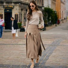 Woman wears pleated skirt, longsleeve top, and heeled sandals. 