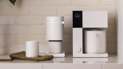 A blocky Fellow Aiden coffee maker in white beside a matching coffee grinder, on a white kitchen counter.
