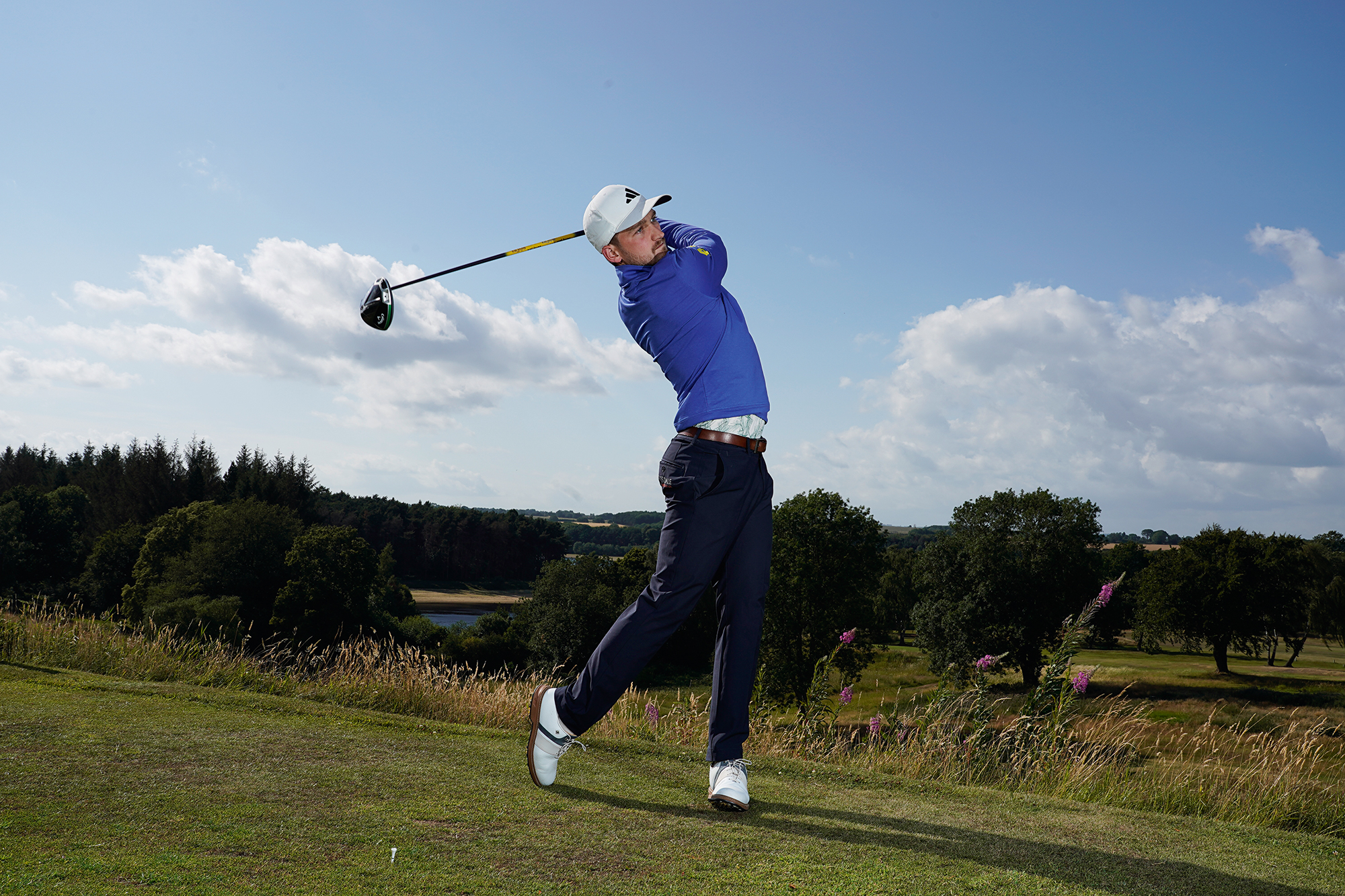Alex Elliott in the finish position with driver, on the 9th tee box at Sand Moor Golf Club overlooking the reservoir and the 16th fairway
