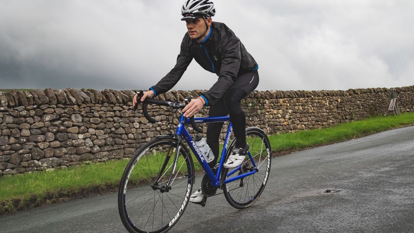 A white man on a blue bike rides with a backdrop of grey skies