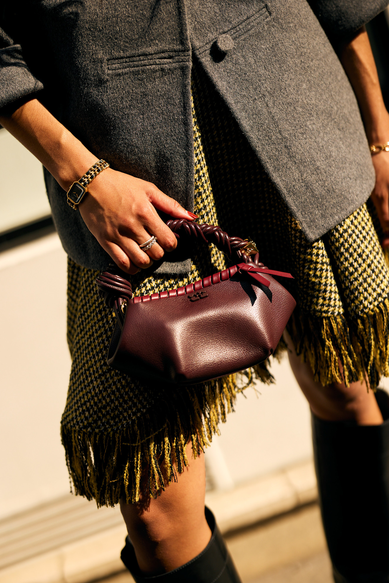 a close up of a woman's hands with red nails holding a maroon bag with a gray jacket