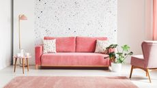 A pink couch in a living room with an accent wall and a pink fluffy rug.