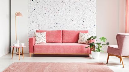 A pink couch in a living room with an accent wall and a pink fluffy rug.