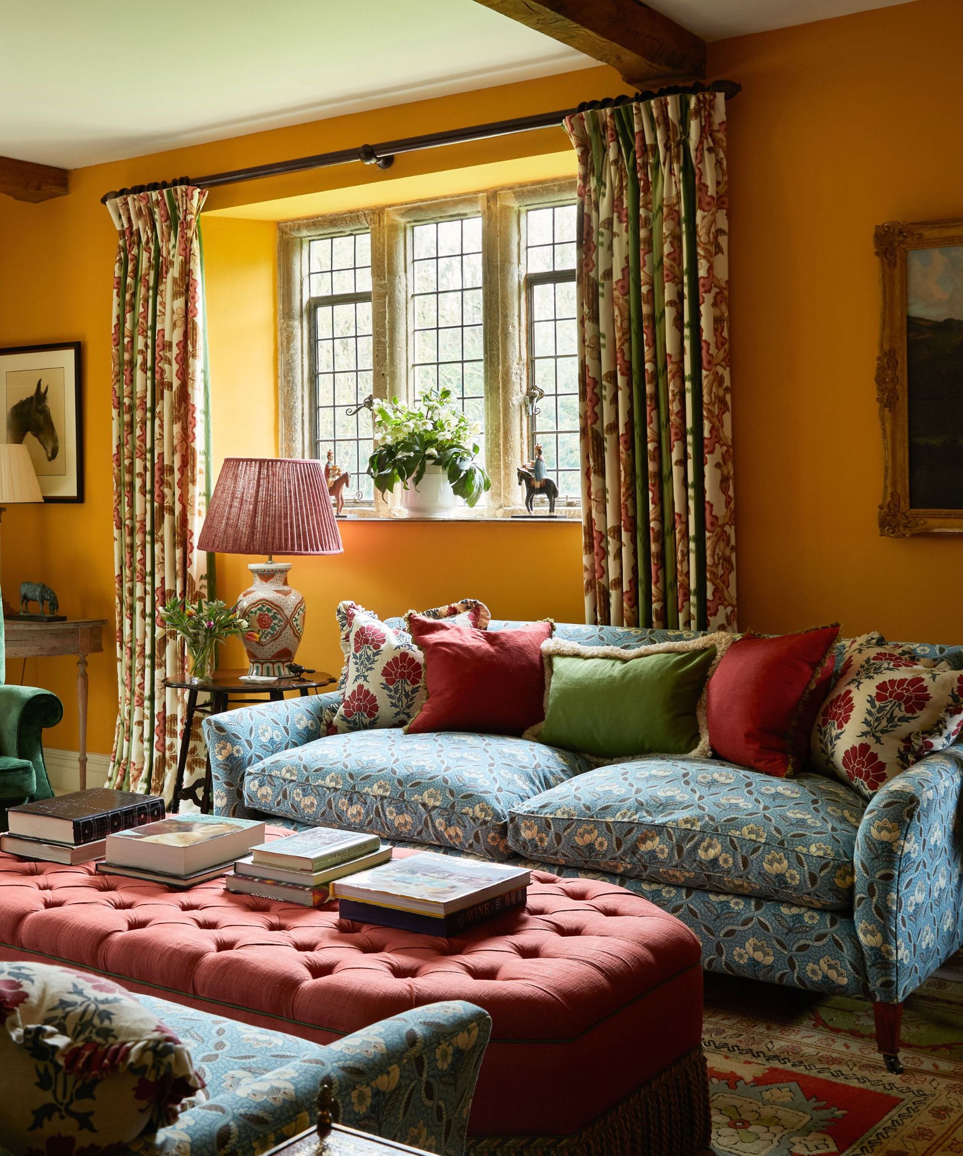 English country home living room in bright yellow with patterned curtains, sofa and a large ottoman