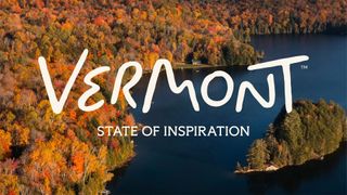 Aerial view of a forested Vermont lake in autumn colours, overlaid with the hand-lettered "Vermont" wordmark and the strapline "State of Inspiration".