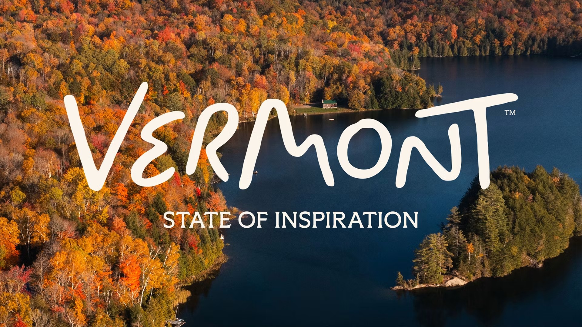 Aerial view of a forested Vermont lake in autumn colours, overlaid with the hand-lettered "Vermont" wordmark and the strapline "State of Inspiration".