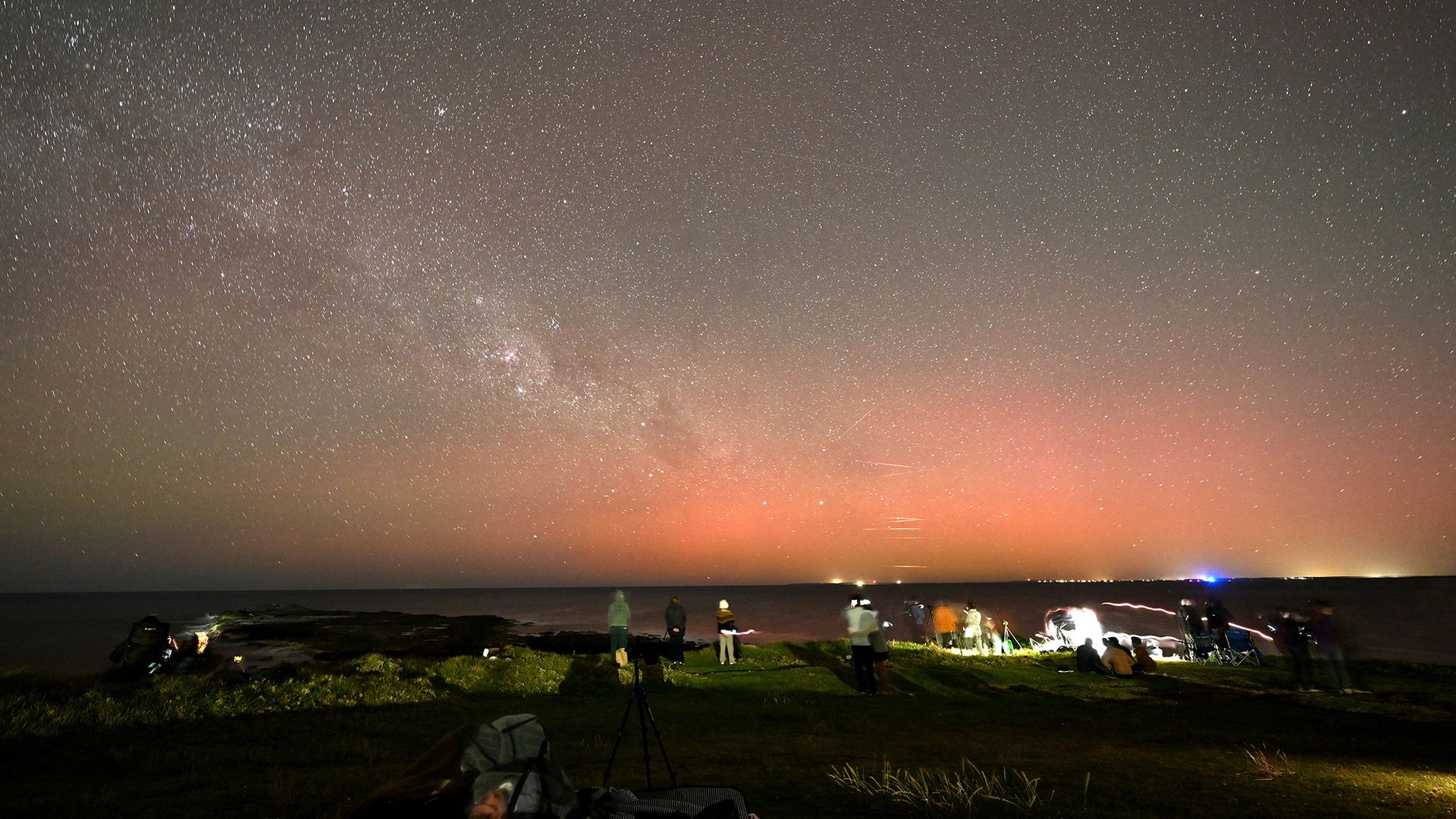 
                                Stargazers gather to watch the Southern Lights illuminating the night sky at Gerroa Headland in Kiama, Australia
                            