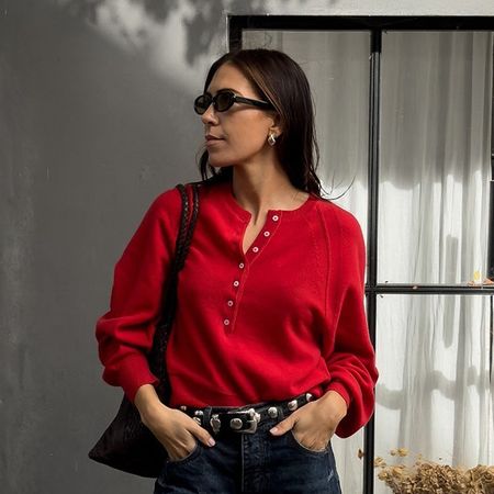 a woman wearing a red sweater, indigo blue jeans, and a brown woven bag