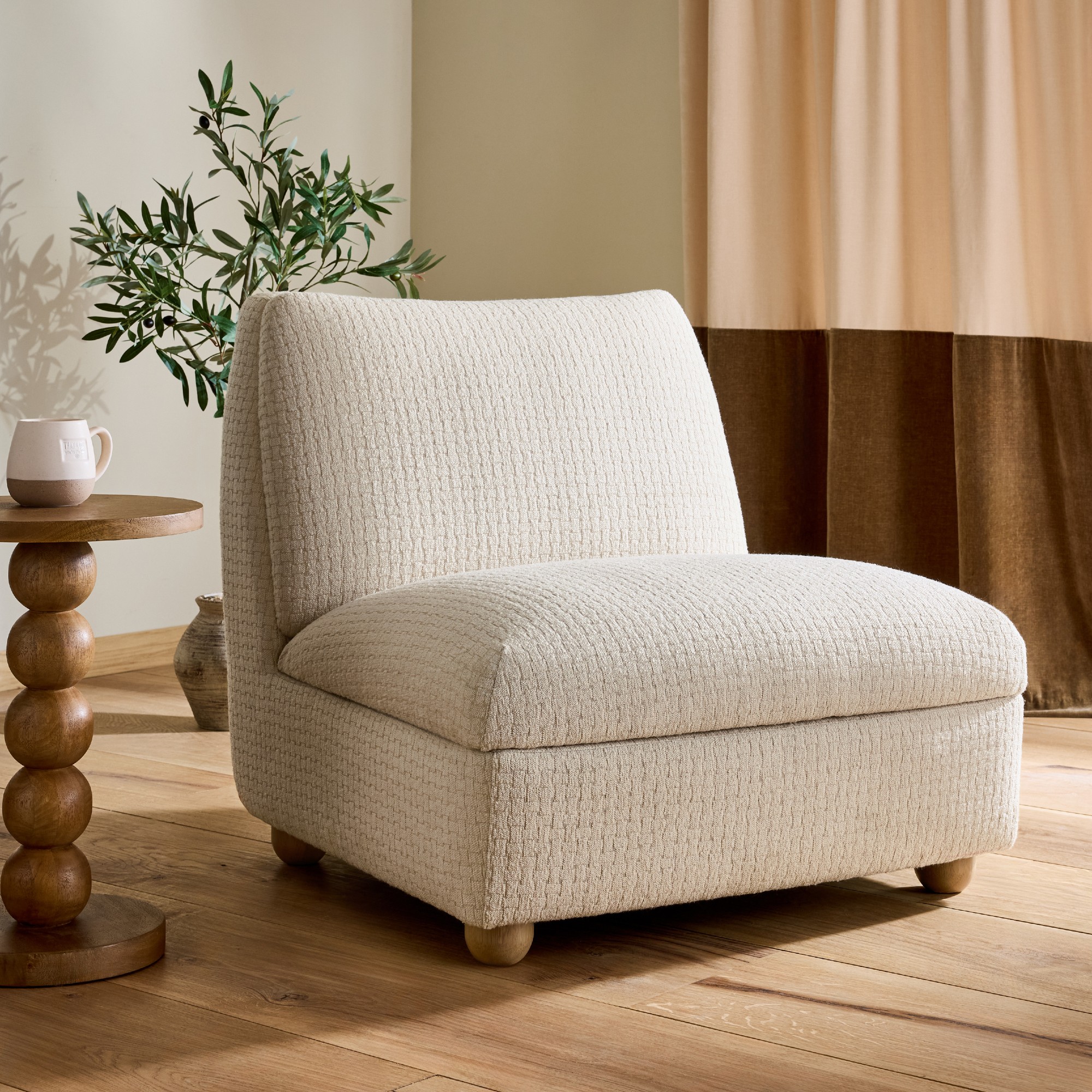Next Clemmie storage accent chair in oyster in a living room with a bobbin side table next to it