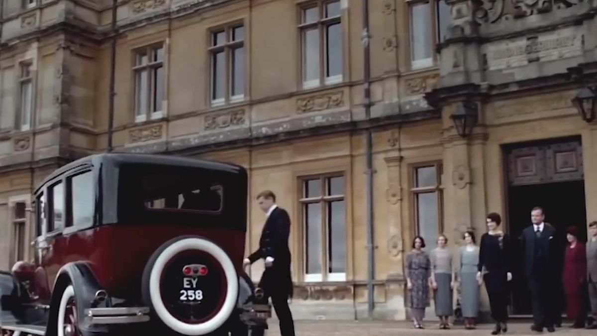 A car pulling up to the front of Downton Abbey with the staff standing in front. 