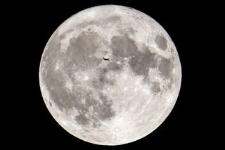 a fully illuminated moon with a small black silhouette of an airplane in the center.